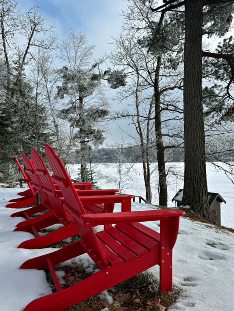 Red adirondack chairs in winter by frozen lake.