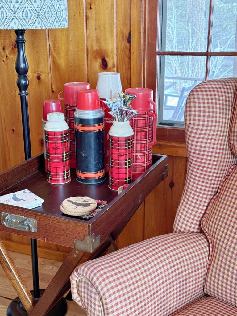 Vintage plaid thermos collection display on side table as cabin decor.