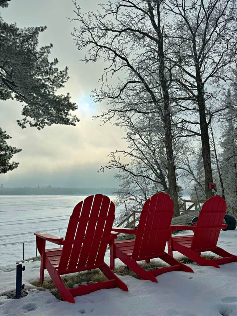 Red adirondack chairs in winter by lake.