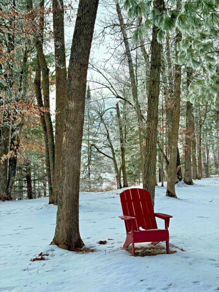 Red adirondack chair in a northwoods winter.