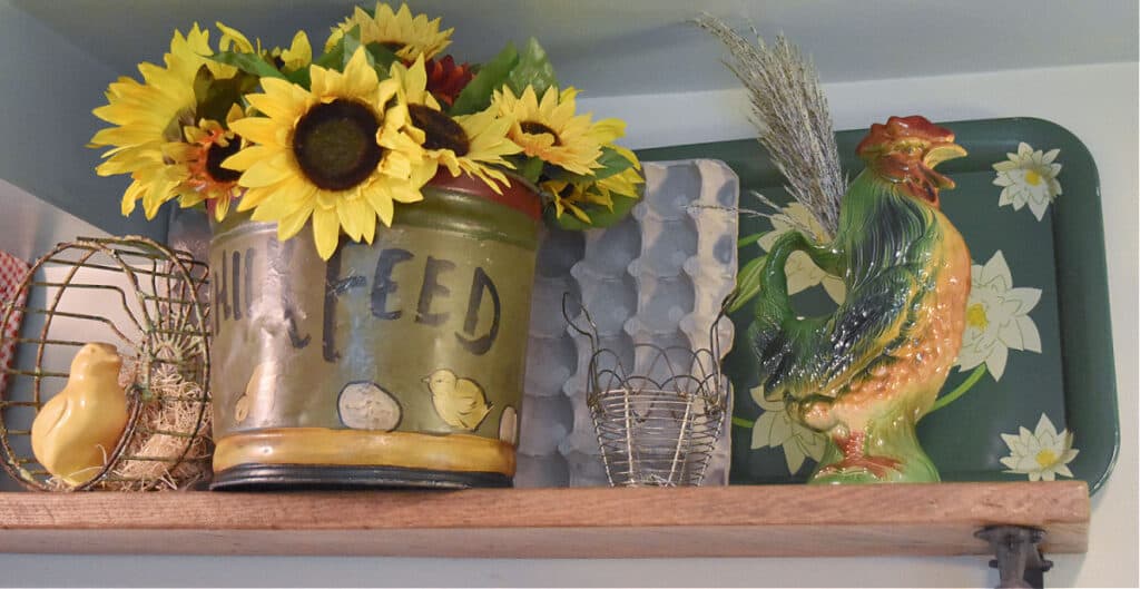 Vintage rooster pitcher on shelf with sunflowers in bucket.