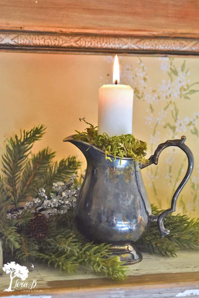 Silver creamer with candle on shelf.