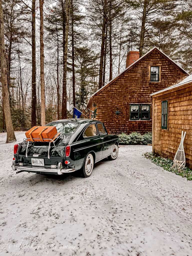 Log cabin and vintage car in driveway with snow.