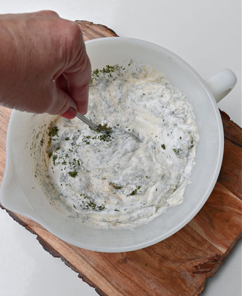 Mixing homemade dill dip in white bowl.