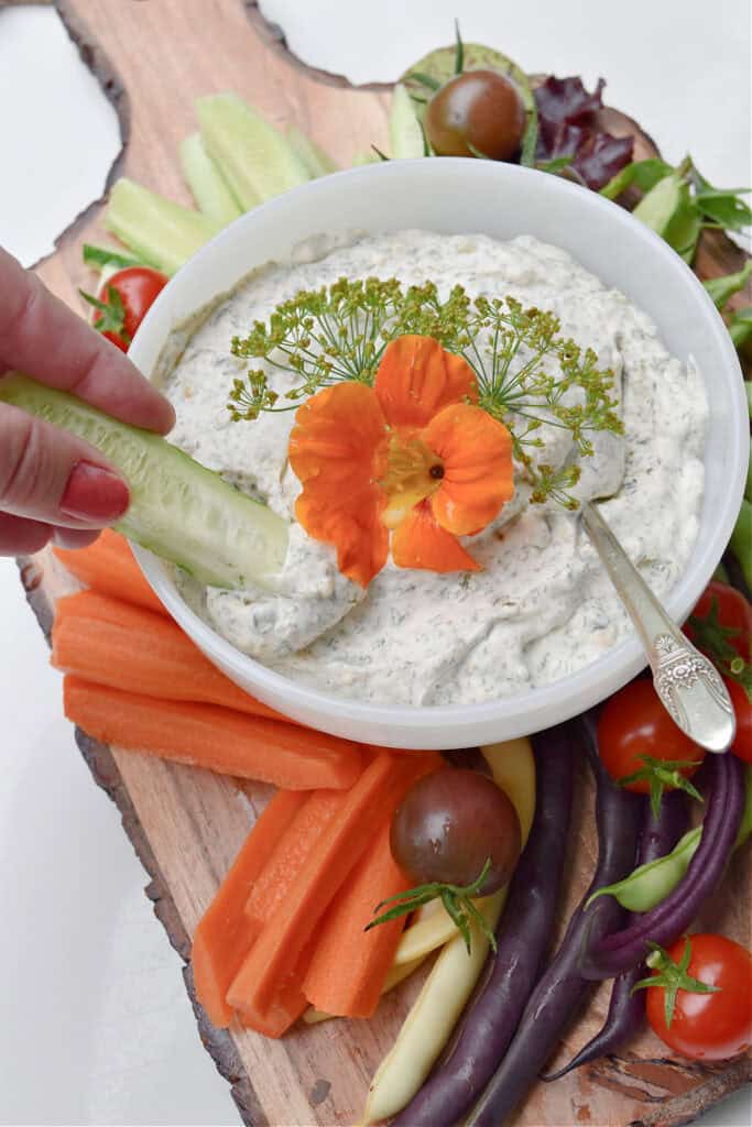 Scooping homemade dill dip with fresh cut veggies on board.