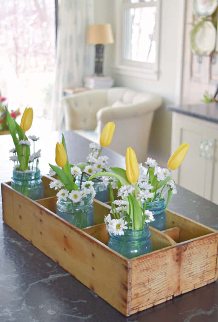 Blue ball jars in wooden caddy with flowers.