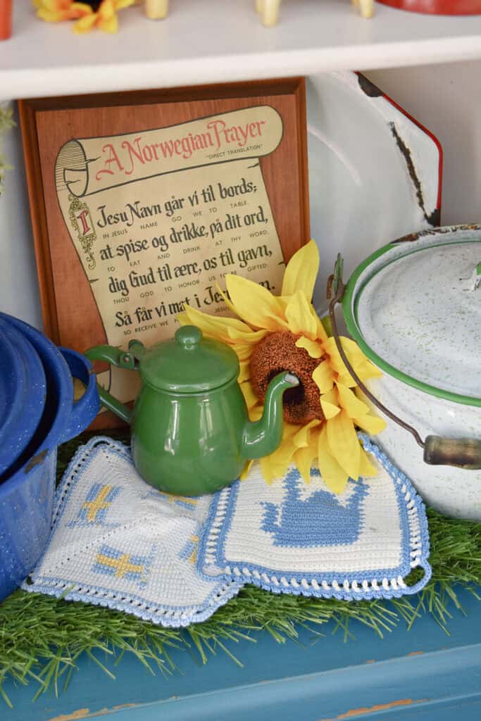 A Norwegian prayer wall art and Swedish hot pads with green teapot.