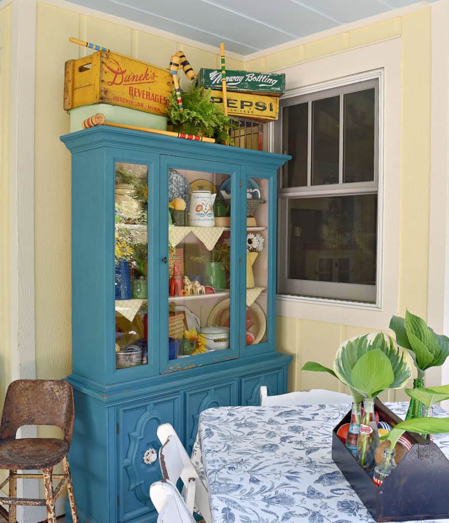Aqua painted hutch on porch with colorful summer time vintage display.