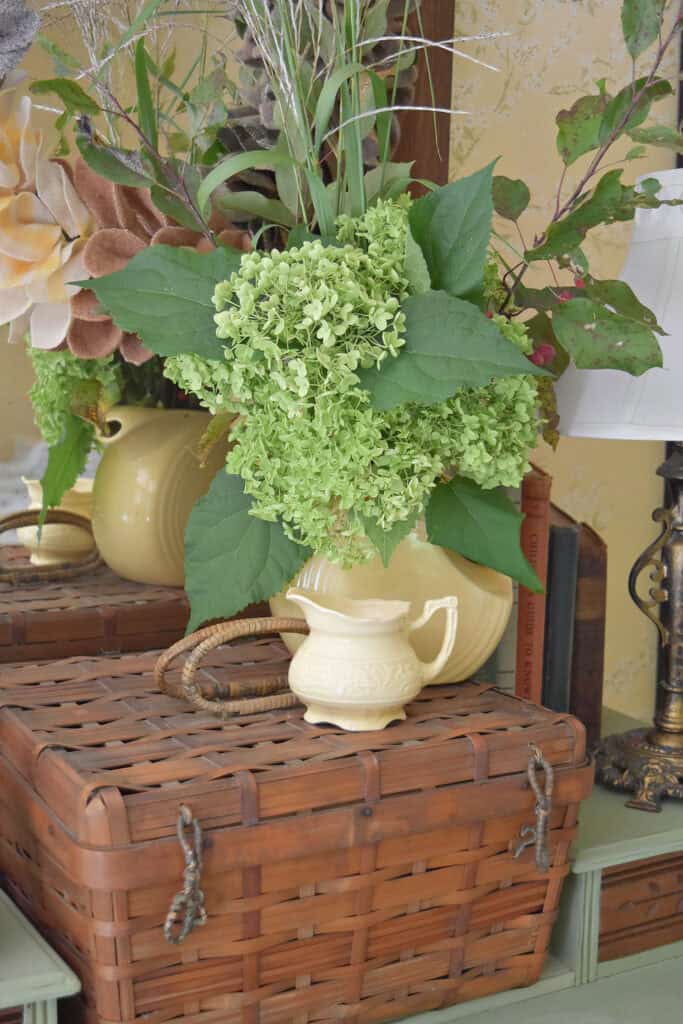 Green hydrangeas in yellow pitcher on vintage basket.