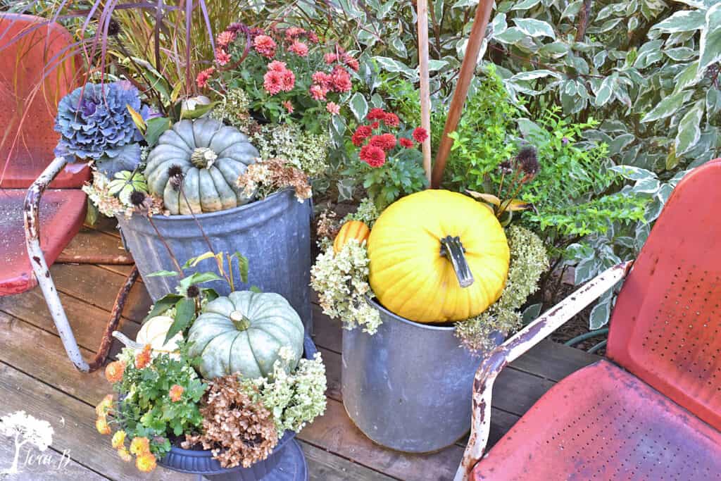 Repurposed metal garbage cans make beautiful outdoor planters on this Fall decorated porch and patio with salvaged style.