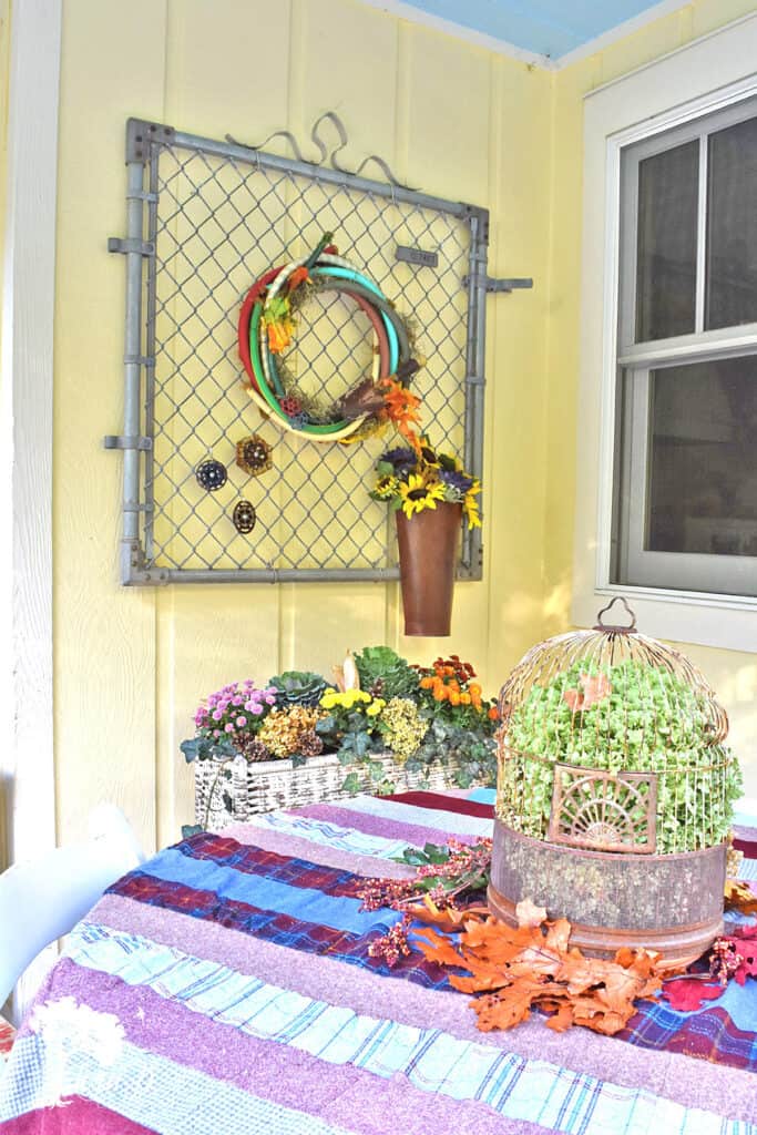 Old garden fence gate is cute with a hose wreath on this fall decorated porch and patio with salvaged style.