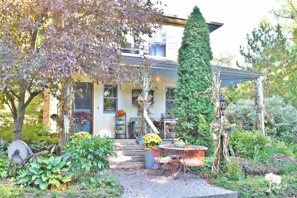 Yellow and white farmhouse with a fall decorated porch and patio with salvaged style.