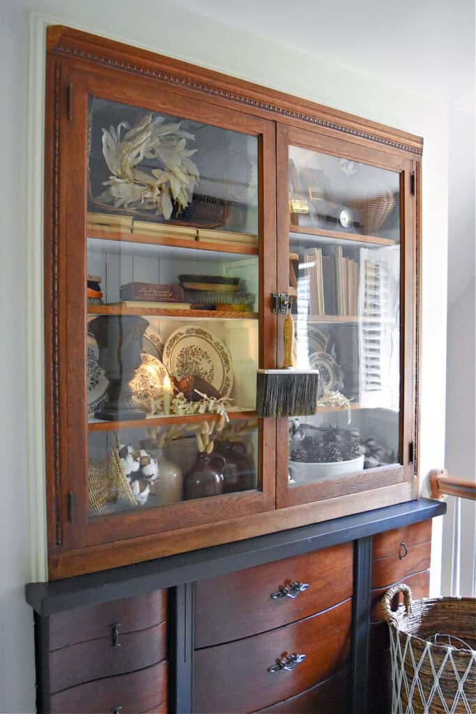 Glass cabinet bookshelf display with old books, transferware and vintage paintbrushes.