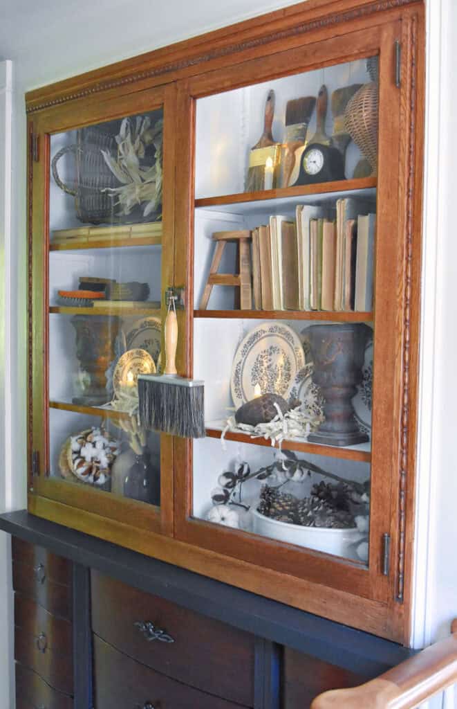 Glass cabinet bookshelf display with old books, transferware and vintage paintbrushes.