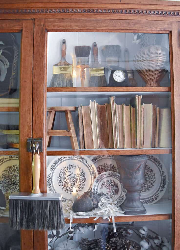 Glass cabinet bookshelf display with old books, transferware and vintage paintbrushes.