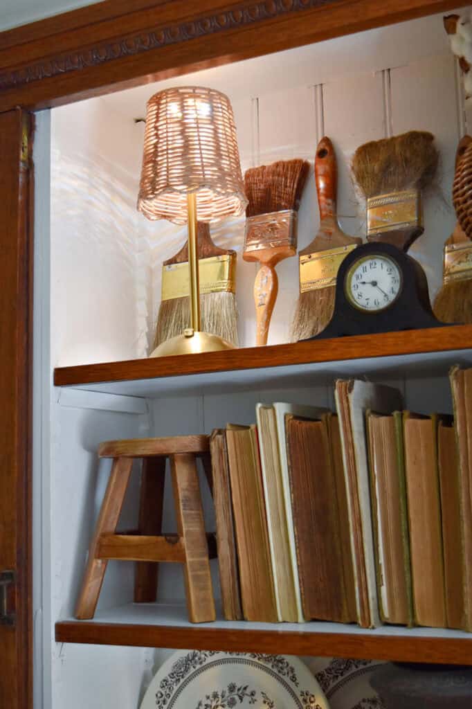 Glass cabinet Fall bookshelf display with old books, transferware and vintage paintbrushes.