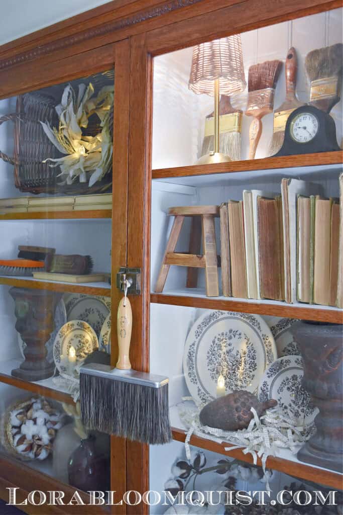 Glass cabinet Fall bookshelf display with old books, transferware and vintage paintbrushes.