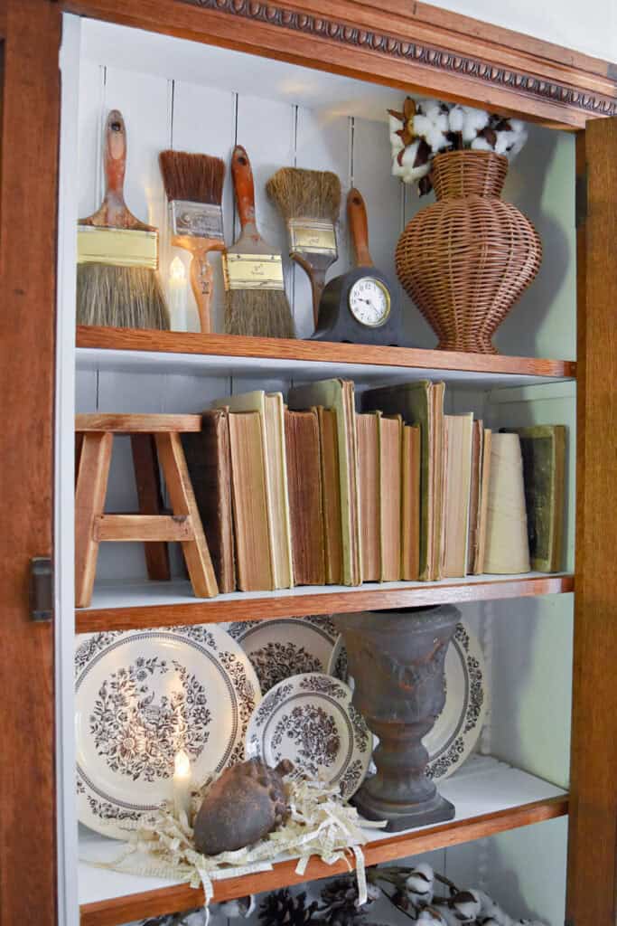 Vintage paintbrushes, old books and brown transferware in a neutral fall bookshelf.