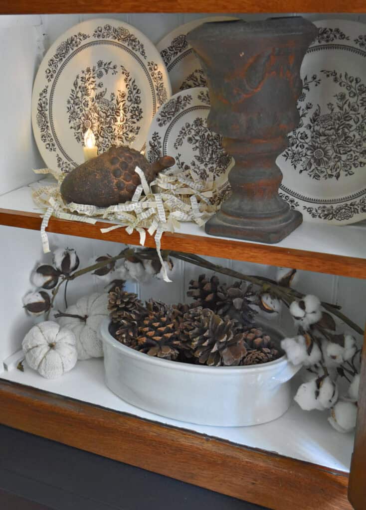 Pinecones, brown transferware and faux cotton add neutral interest in a fall bookshelf display.