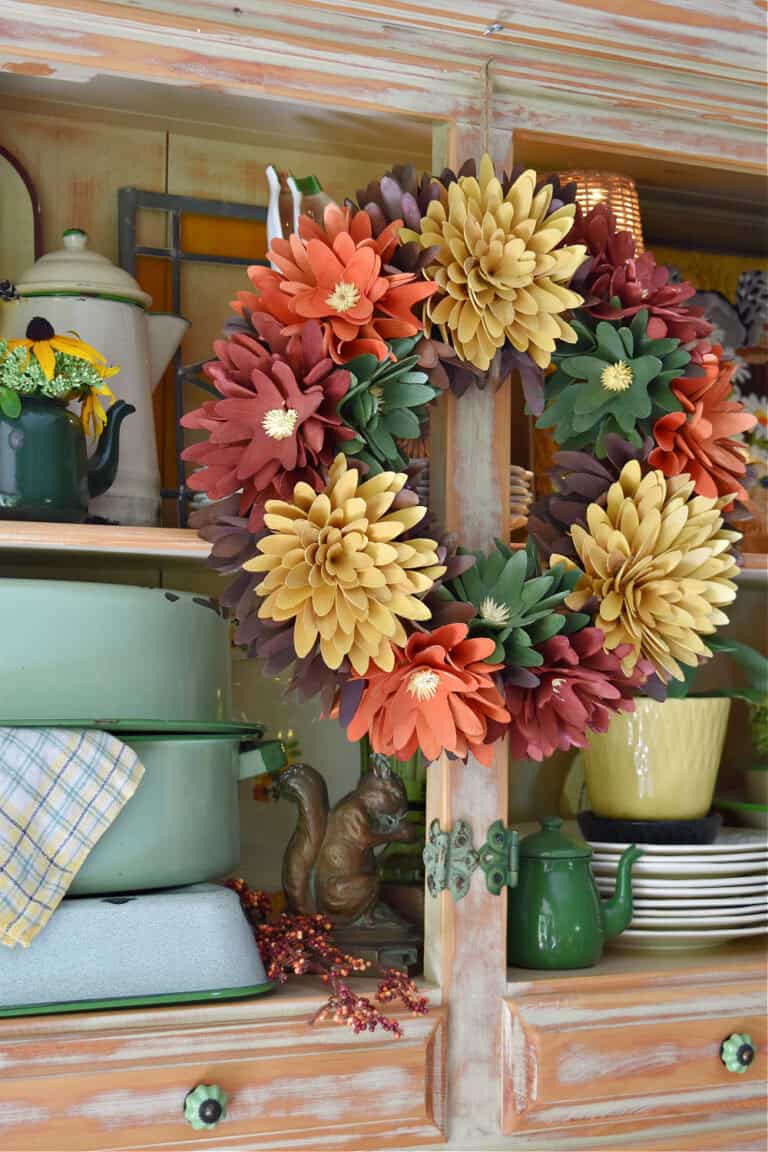 Fall colored flower wreath hanging on hutch.