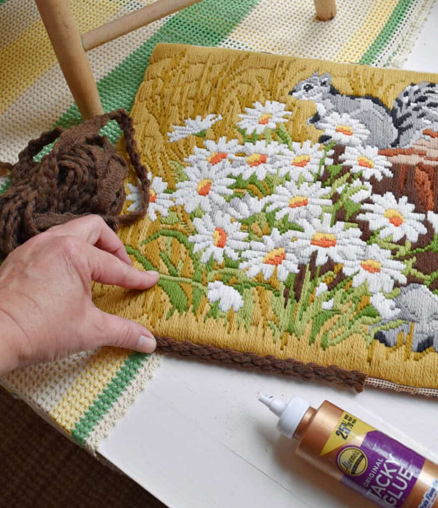 Glueing brown trim onto vintage needlepoint.