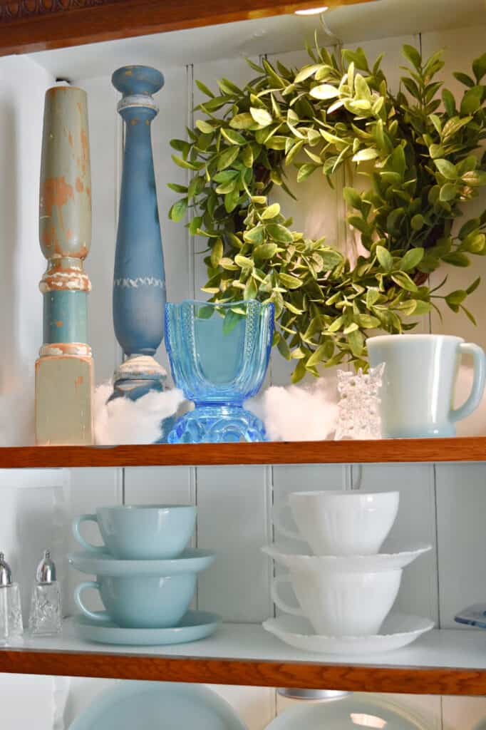 Milkglass cups and saucers stacked on winter decorated shelves.