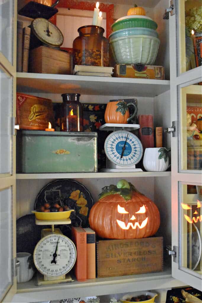 Vintage scales and mixing bowls in a Halloween cupboard display.