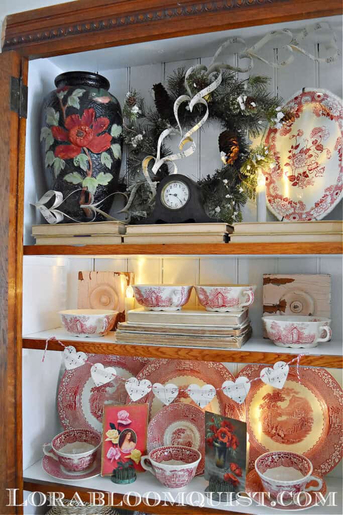 Vintage Valentines Decorations in glass front antique bookshelf with DIY paper heart garland,