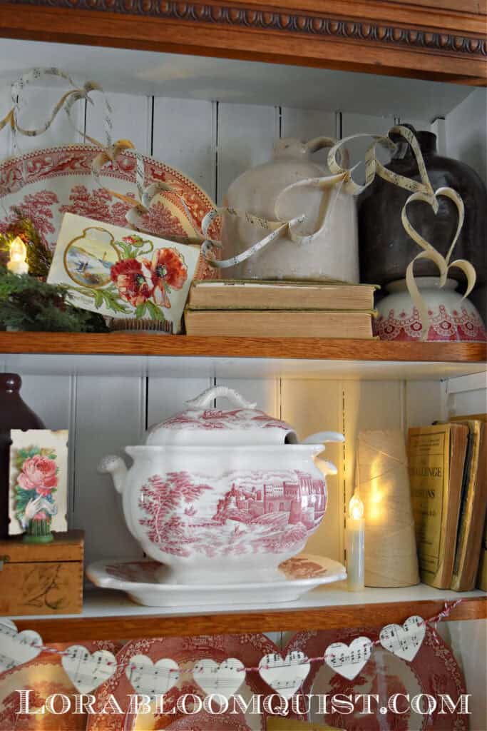 Vintage Valentines Decorations in glass front antique bookshelf with DIY paper heart garland,