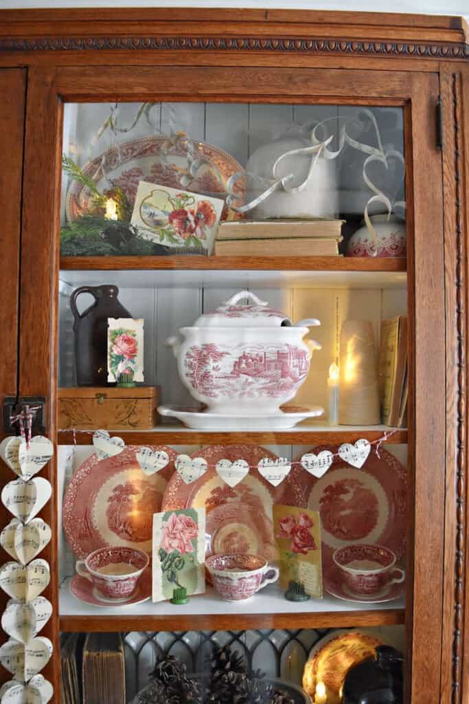 Vintage Valentines Decorations in glass front antique bookshelf with DIY paper heart garland,
