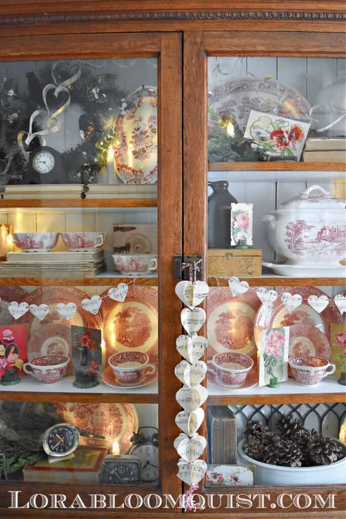 Vintage Valentines Decorations in glass front antique bookshelf with DIY paper heart garland,