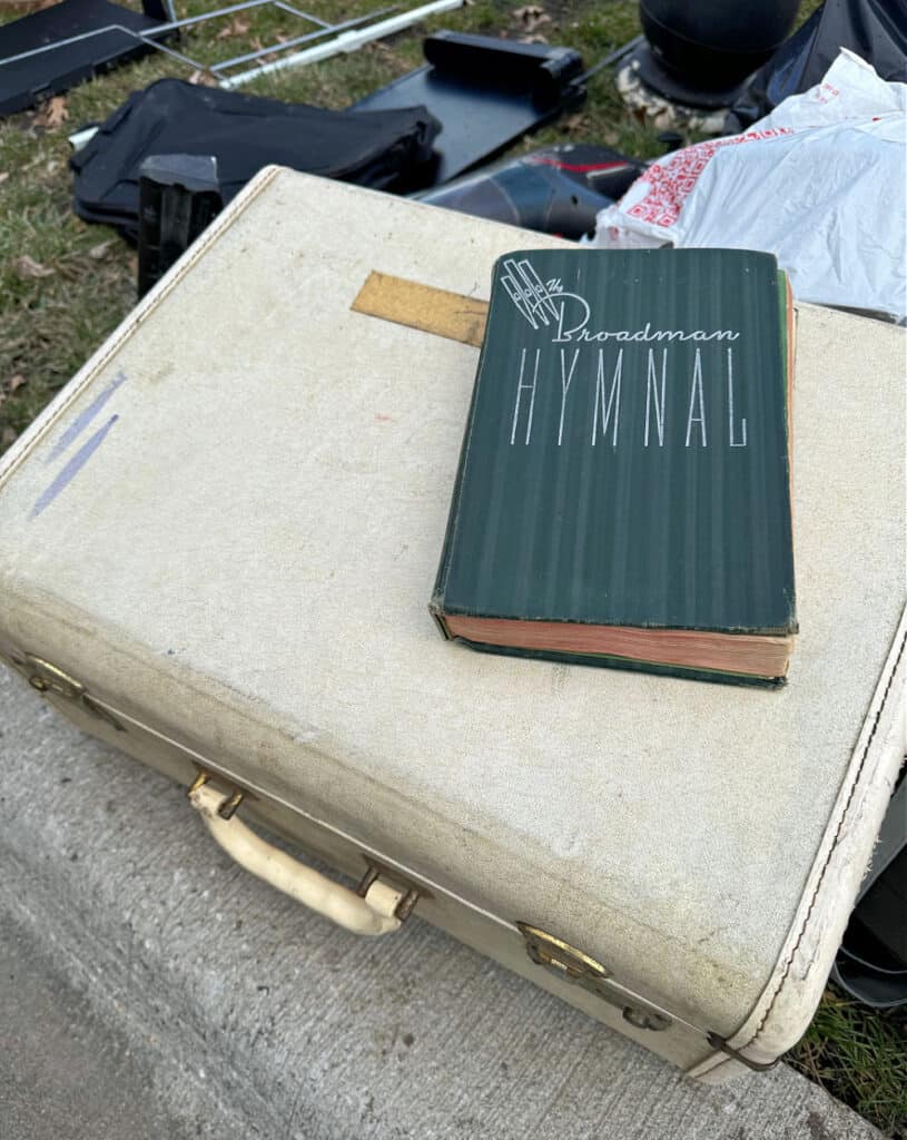 Old hymnal and vintage suitcase in curbside pile.