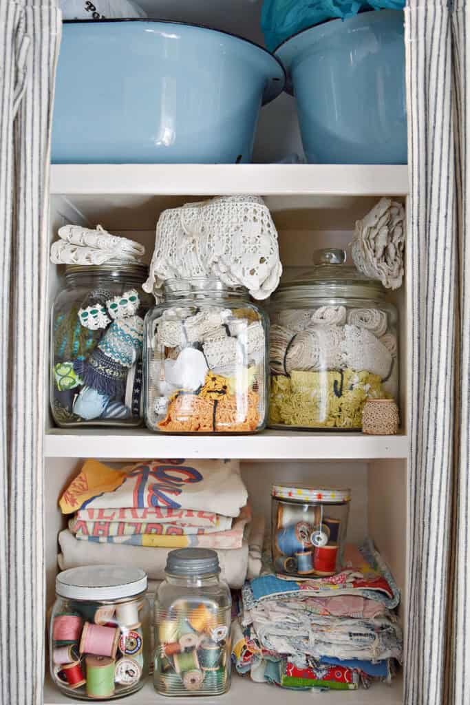 Craft room shelves with vintage lace collection, grain sacks, old quilts and colorful thread.
