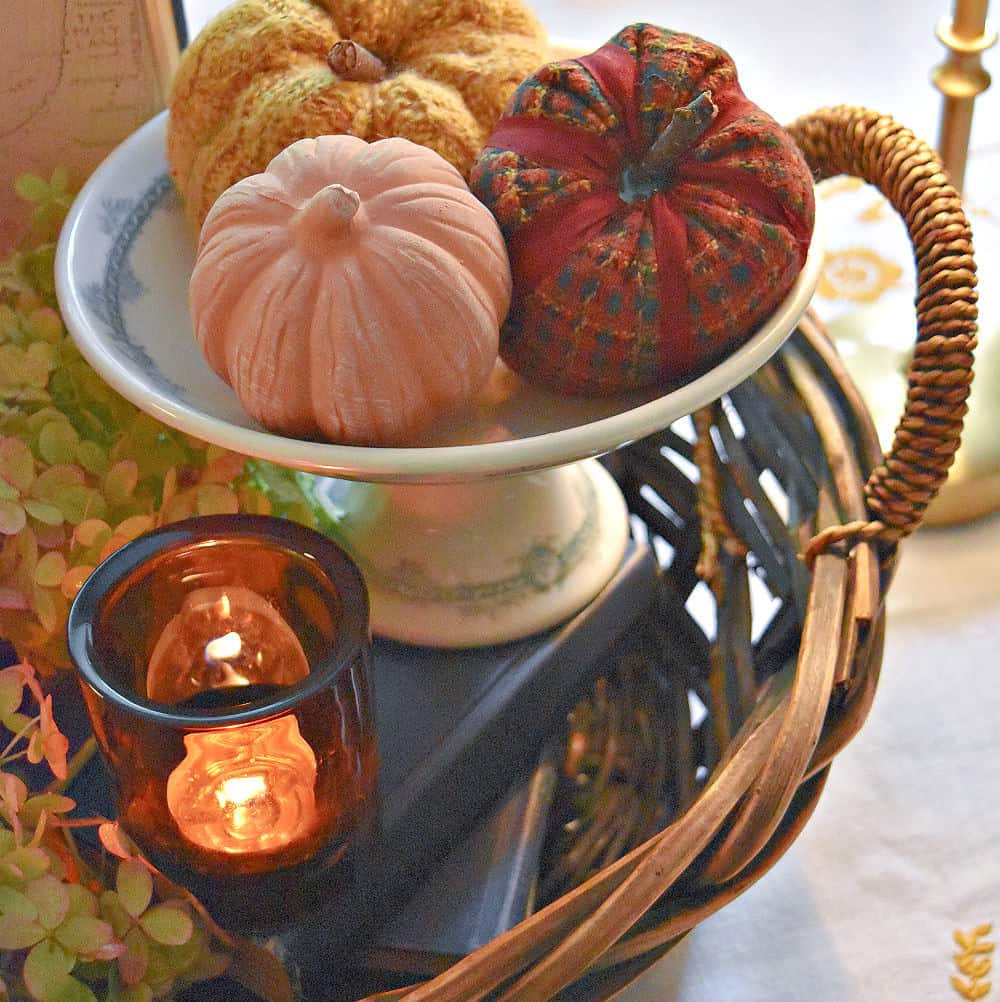 Small pumpkins in ironstone pedestal and amber glass candle as Fall centerpiece.