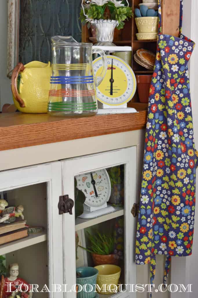 Colorful retro apron and vintage finds decorate a kitchen cupboard display.