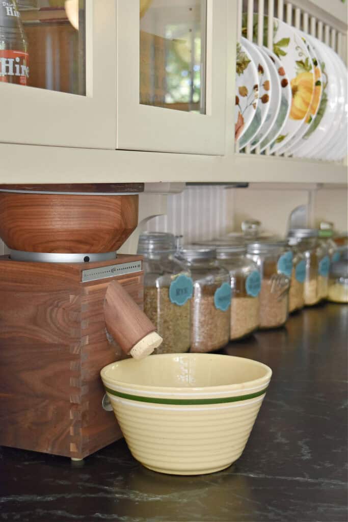 Komo classic grain mill on kitchen counter with grains in glass jars.