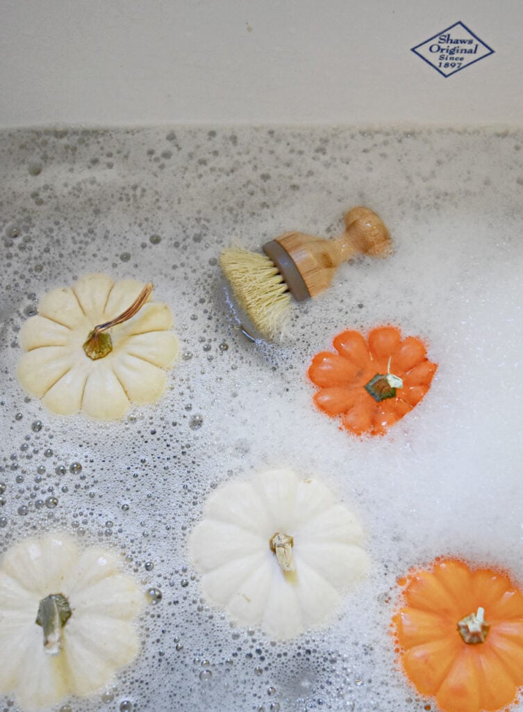 Washing mini pumpkins in soapy sink.