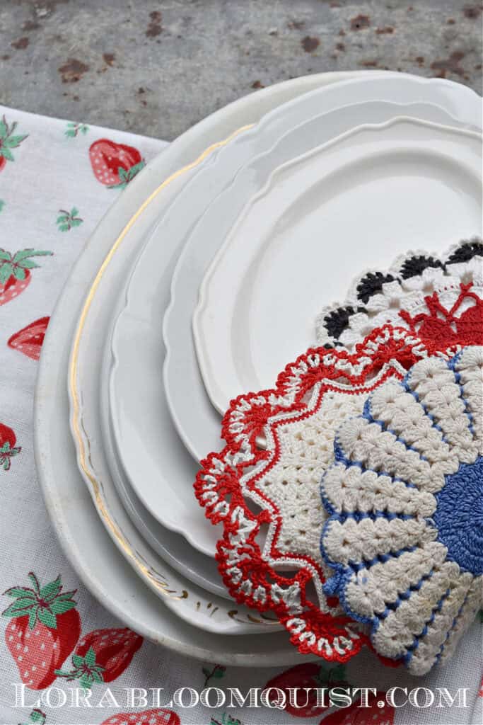 Stack of white ironstone platters and vintage crochet hot pads.