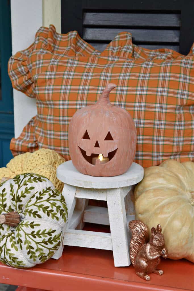 Terra cotta jack o lantern on white stool with decor pumpkins around.