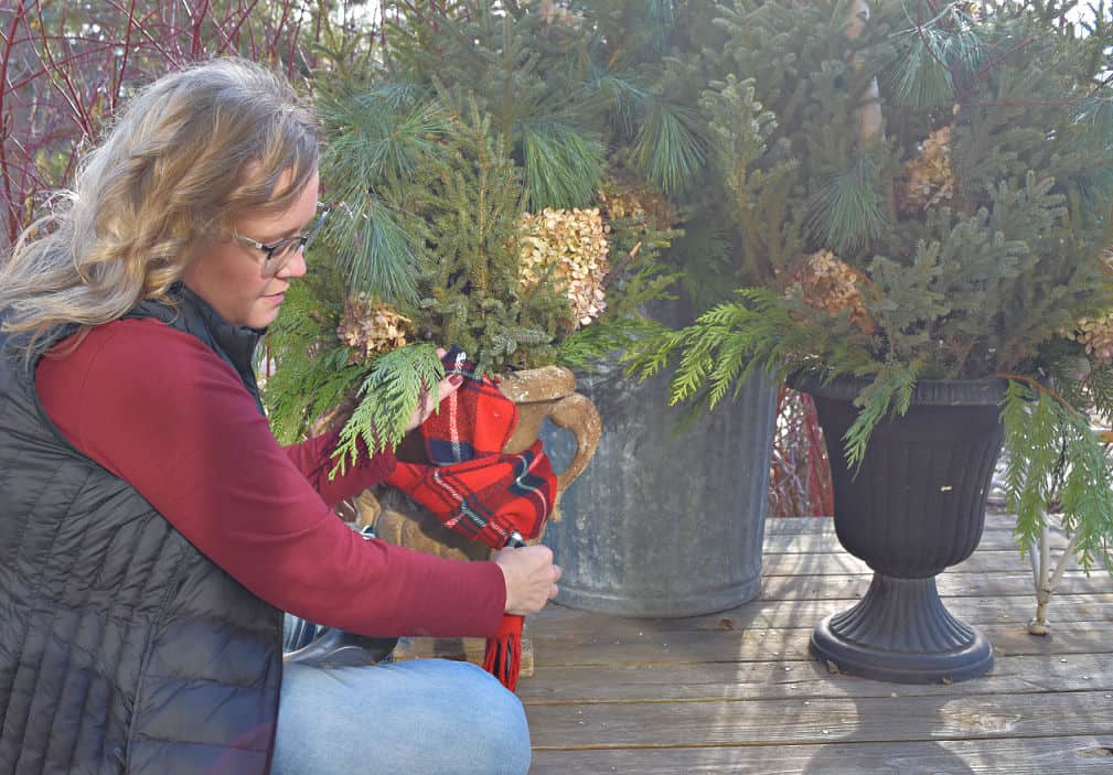Showing how to decorate a winter planter with a plaid scarf.