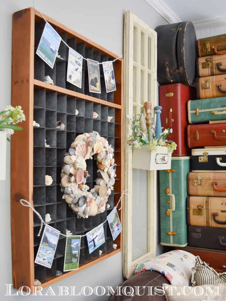 DIY seashell wreath displayed with vintage suitcases and travel postcard banner.