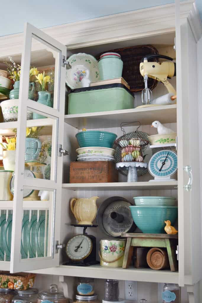 Farmhouse glass kitchen cupboard decorated with vintage finds.