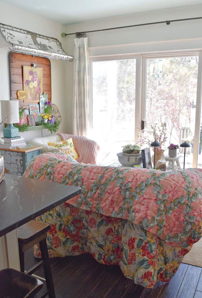 Cozy kitchen sitting area with vintage floral quilt and Spring painted art.