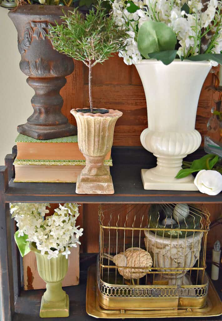 Classic footed planter containers fill a Spring decorated bookshelf.