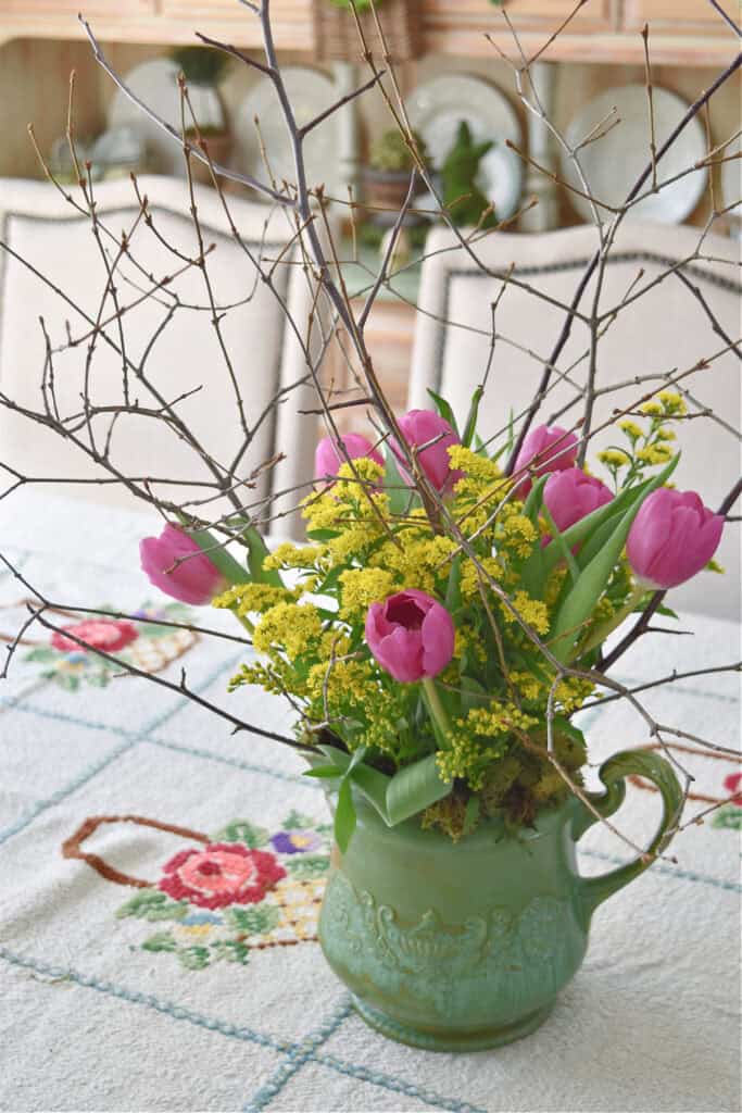 Pink tulips and yellow flowers in green pitcher.