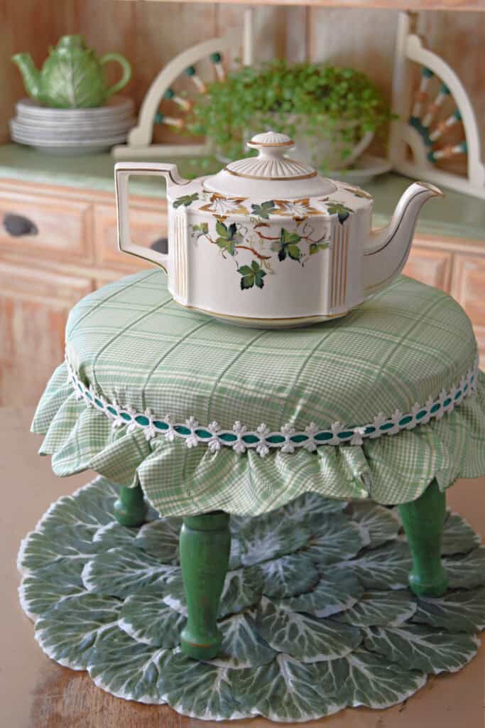 Vintage green upholstered cottage footstool with teapot.