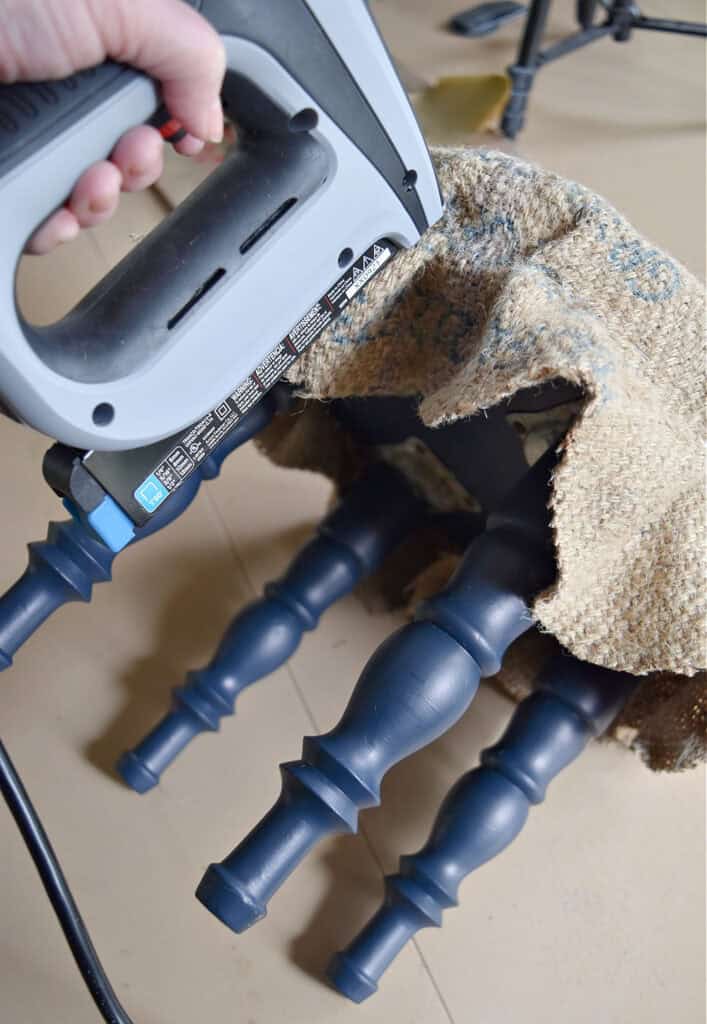 Stapling burlap on old footstool for makeover.