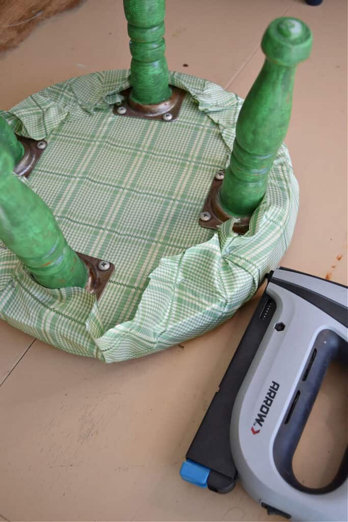 Stapling fabric onto old footstool for makeover.