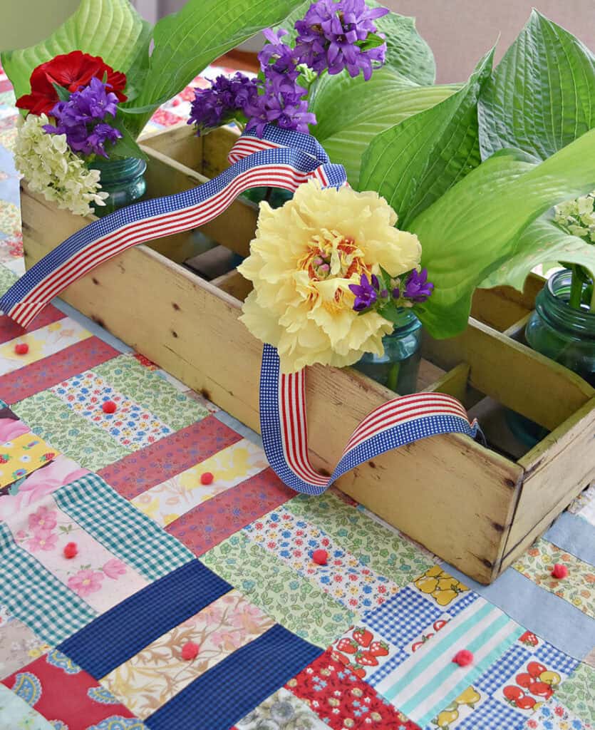 Summer centerpiece with vintage patchwork quilt, backyard flowers in tool caddy.