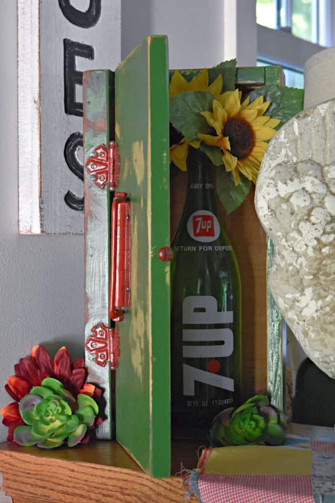 Green glass 7 up bottle with flowers in old box.
